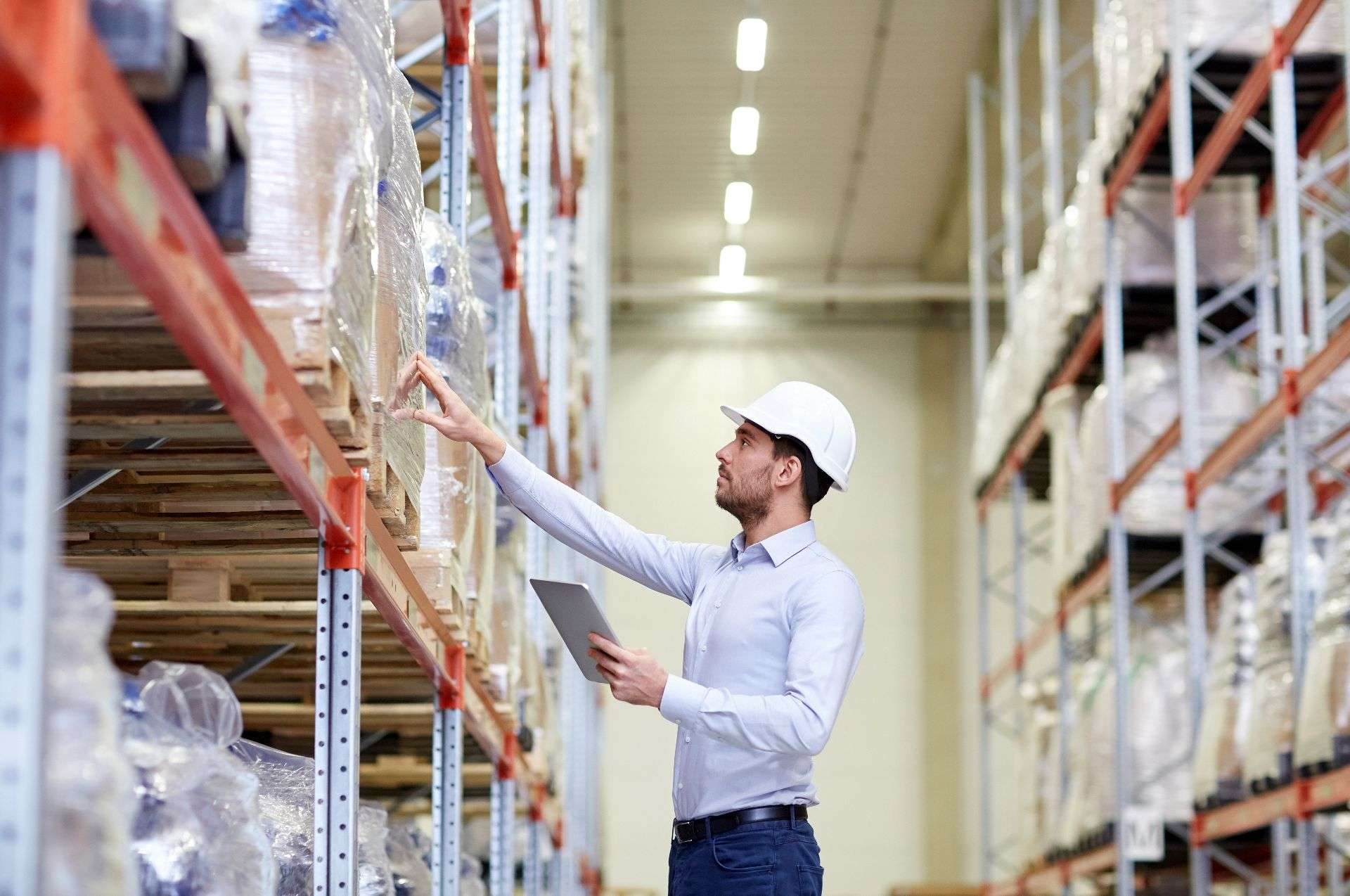 Warehouse worker inspecting inventory on shelves, wearing a hard hat and holding a tablet, representing logistics and inventory management services in Jacksonville by Skinner Moving & Storage.