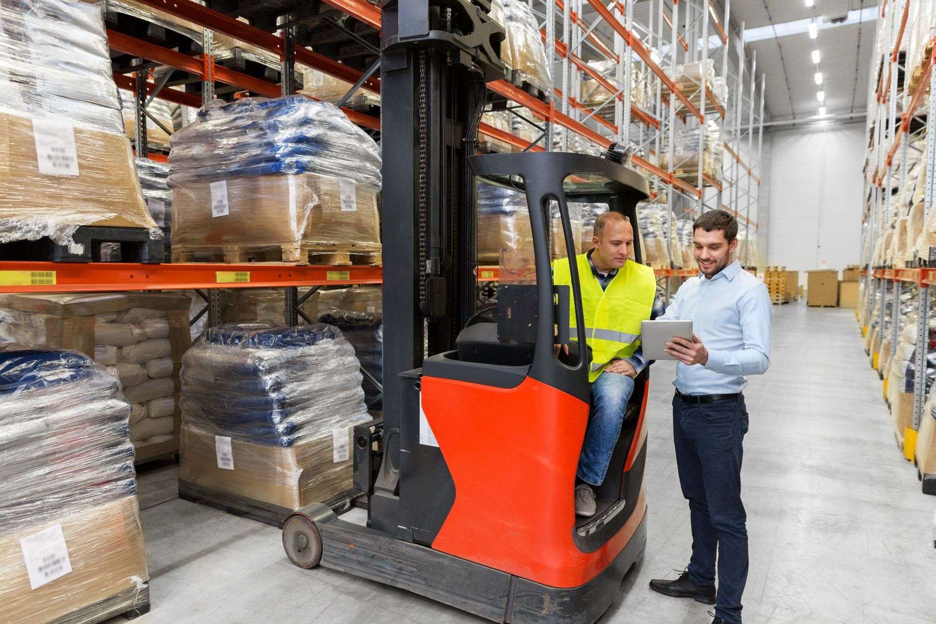 Warehouse workers discussing logistics on a forklift in a storage facility, surrounded by pallets of goods, highlighting efficient inventory management for Jacksonville warehousing services.