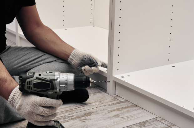 Person using a power drill to assemble white shelving units, demonstrating careful installation for valuable items in a home or office setting.