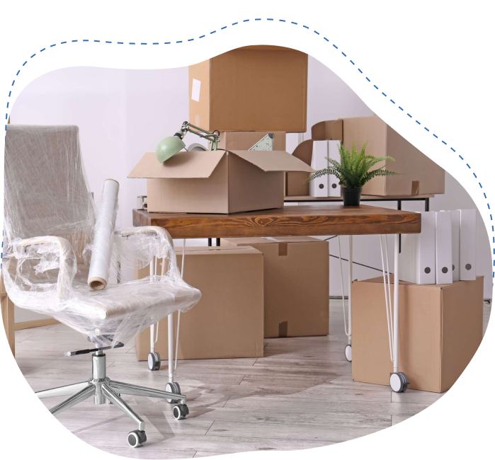 Office relocation scene with unpacked cardboard boxes, a wooden desk, a wrapped office chair, and a green plant, illustrating the moving process for businesses.