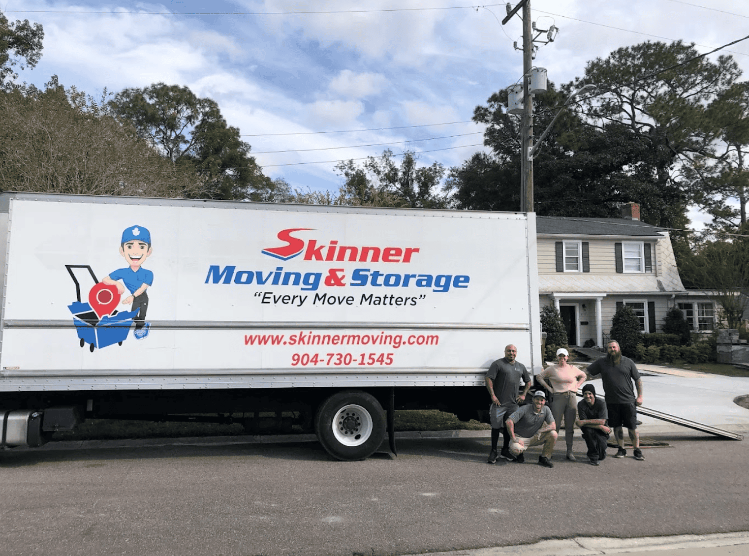 Five Skinner Moving & Storage crew members posing together in front of their branded moving truck on a Jacksonville residential street